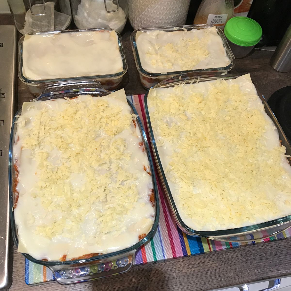 4 prepared lasagnes in glass dishes on a kitchen counter top waiting to be cooked