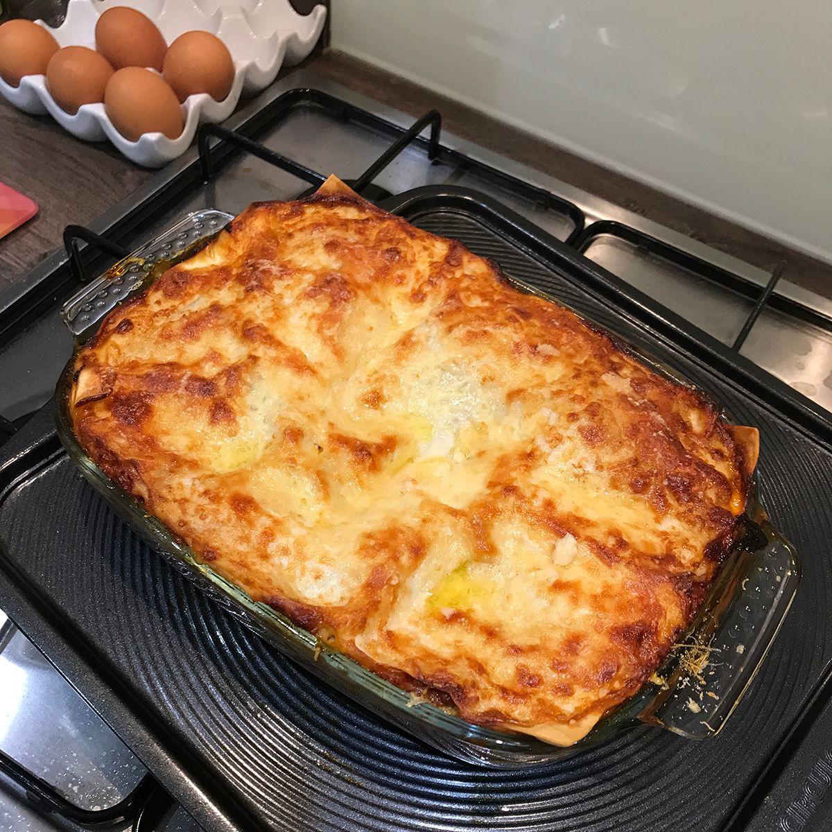 A just-cooked lasagne in a glass dish on a baking tray on top of a cooking hob