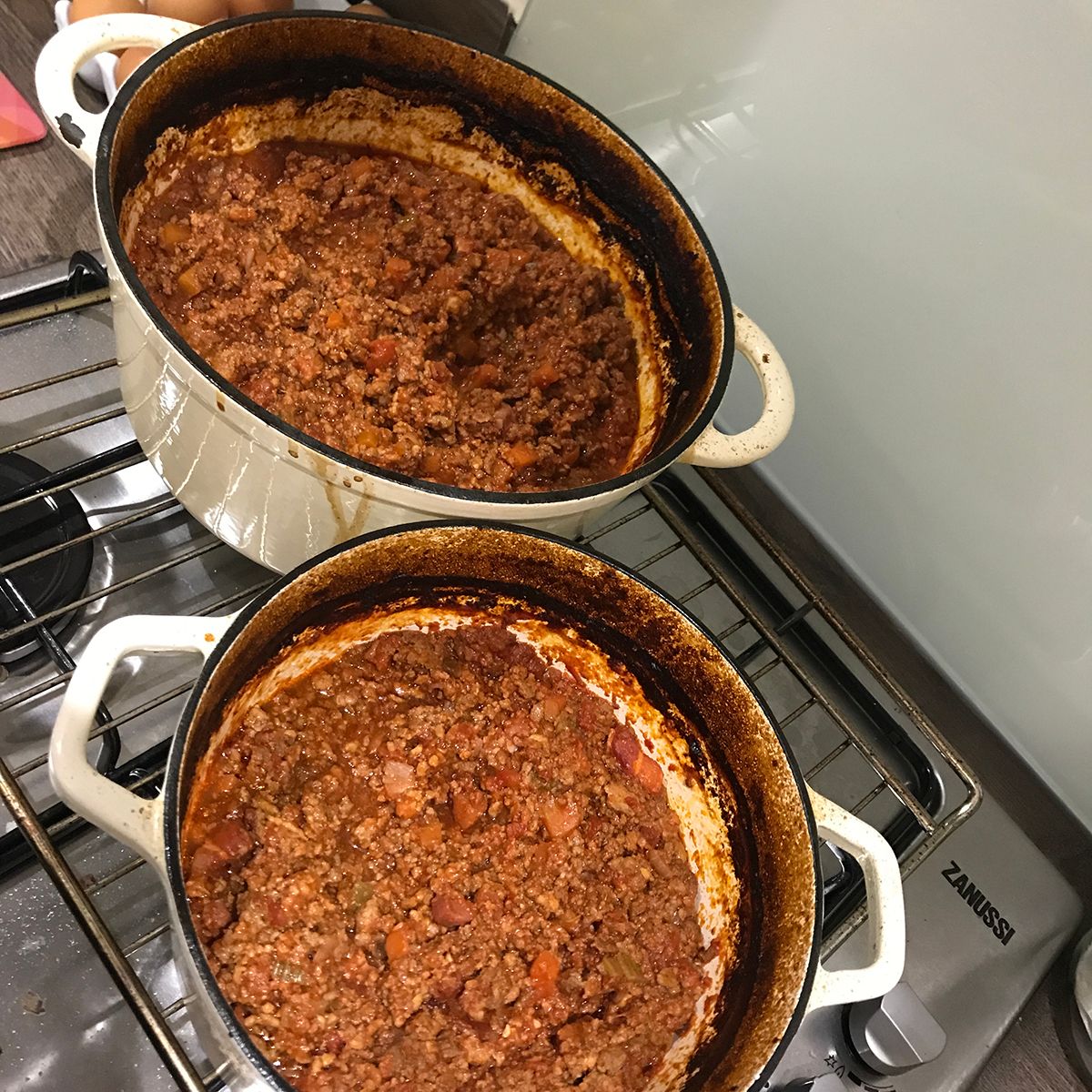 Two cast-iron casseroles filled with cooked lasagne 'meat sauce' on top of a cooking hob