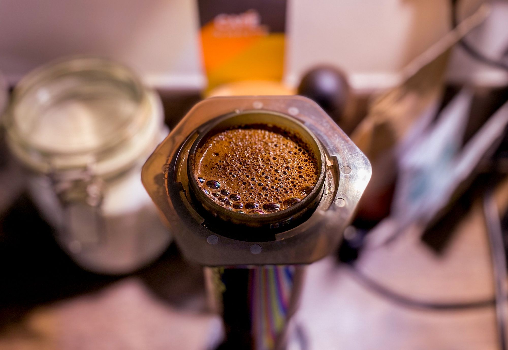 A close-up macro shot of coffee brewing in an Aeropress in the inverse method with a sugar jar and other kitchen items blurred in the background