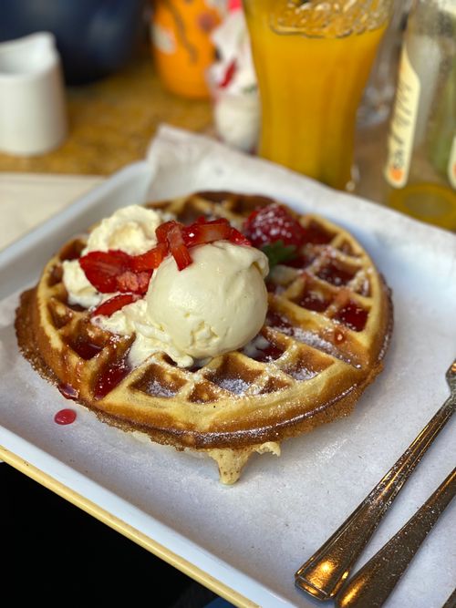 A crispy waffle topped with ice cream, a few strawberries and whipped cream